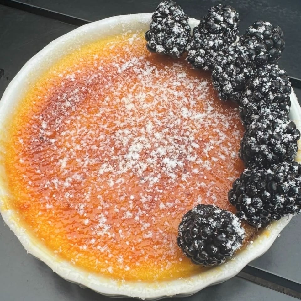 Caramelized custard tart dusted with powdered sugar and topped with fresh blackberries.