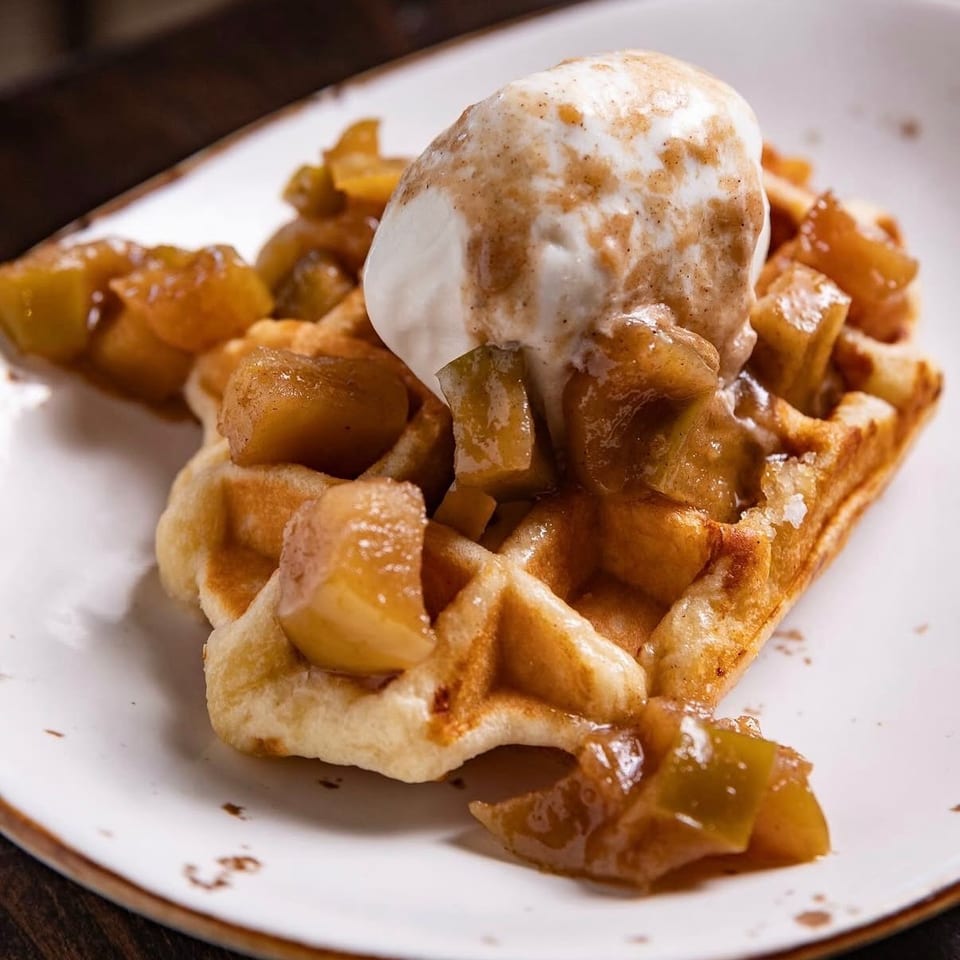 Golden waffle topped with caramelized apples and a scoop of vanilla ice cream on a white plate.