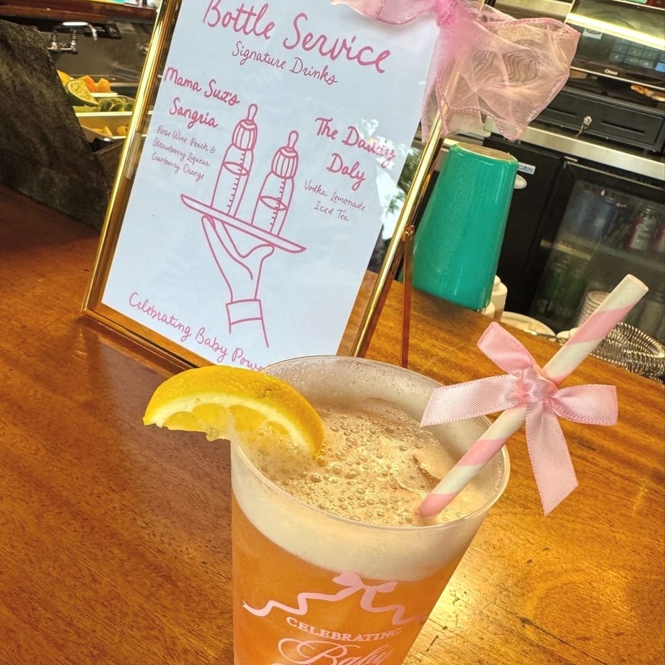 Frosted orange cocktail garnished with a lemon wedge and pink-striped straw beside a signature drinks menu at a bar.