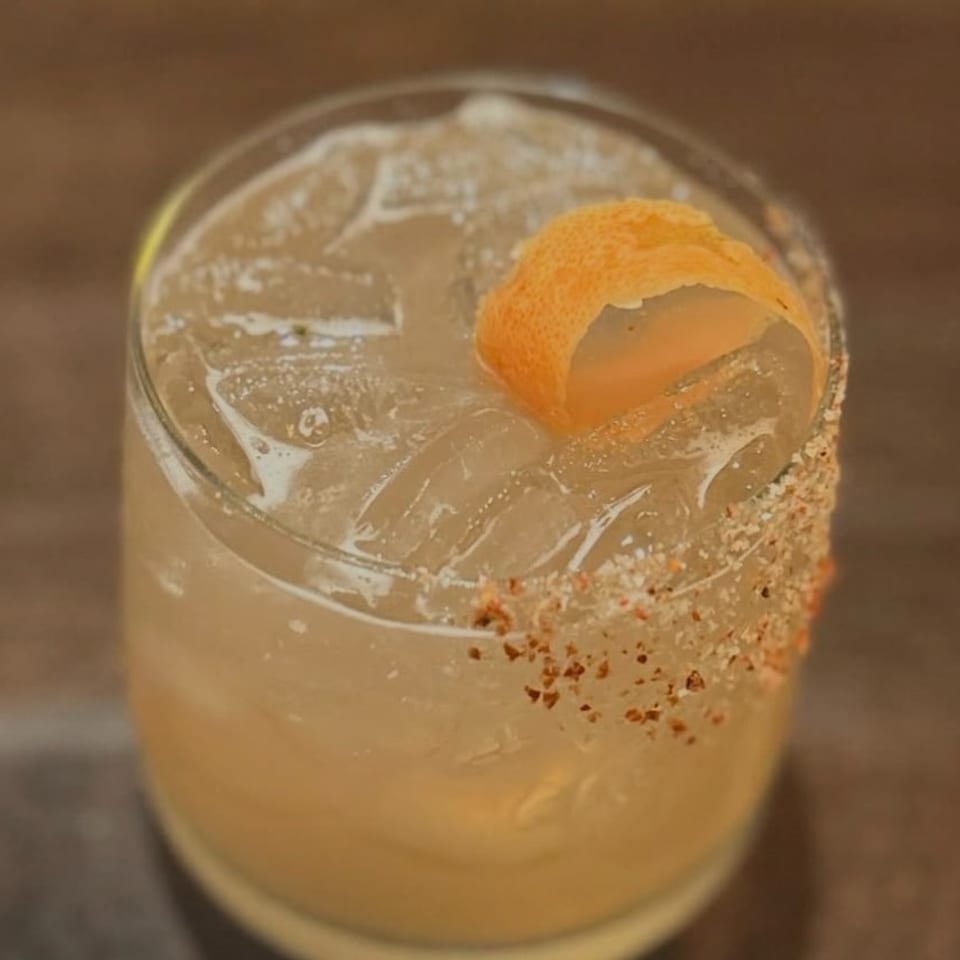 Citrus cocktail with ice, an orange peel garnish, and a spiced rim served in a short glass.